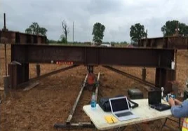 Construction site with steel beams and surveying equipment under cloudy sky.