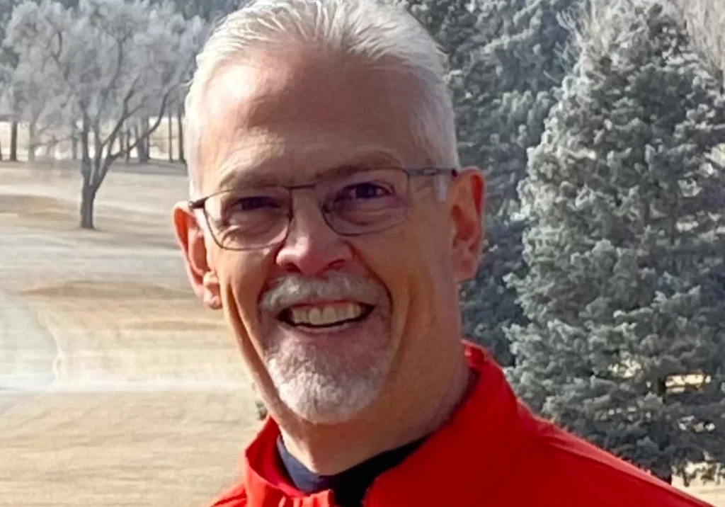 Smiling elderly man in glasses and red jacket outdoors.